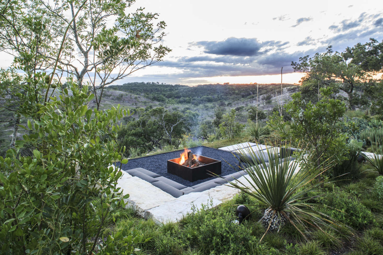 Sectional seating by Gloster has a low profile to focus attention on the fire pit. A permeable black gravel patio surrounds the pit.