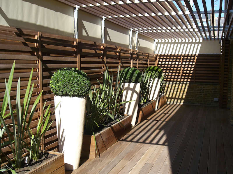 UK garden designer Richard Miers designed a side trellis for a private courtyard with stretched sailcloth panels at top. Above the courtyard, a wooden screen blocks higher, adjacent apartments from looking straight in.