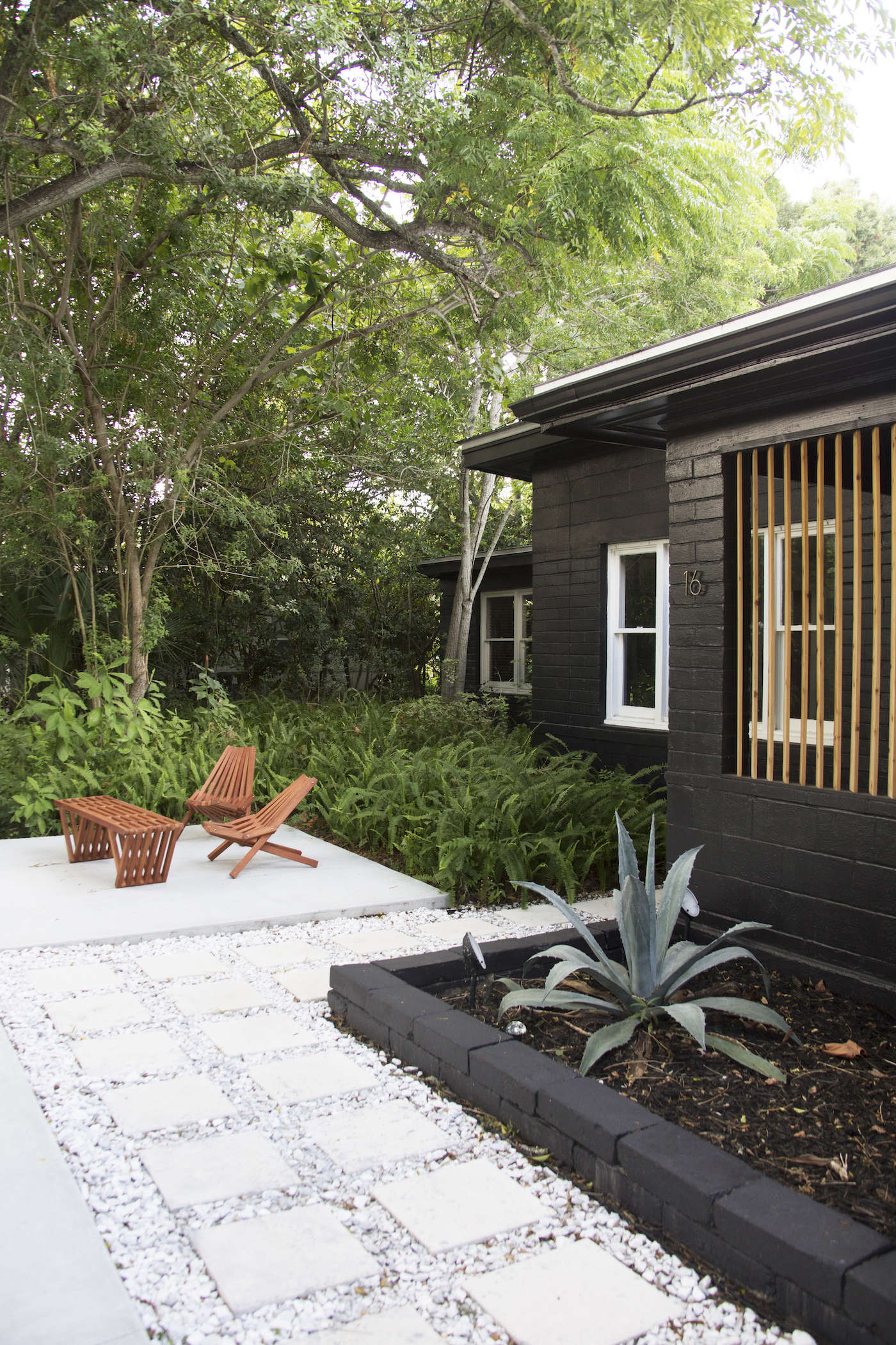 The couple replaced an unkempt entry patio and lawn with a small planting bed edged with painted brick. They built a permeable path of concrete pavers (from Home Depot), set in gravel to aid drainage.