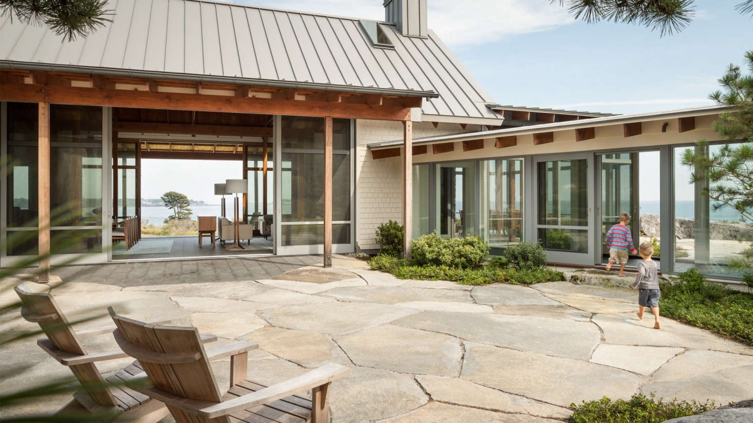 A glass walkway connects the main living volume to the bedroom wing. Sliding glass doors link the courtyard to the fire pit beyond.