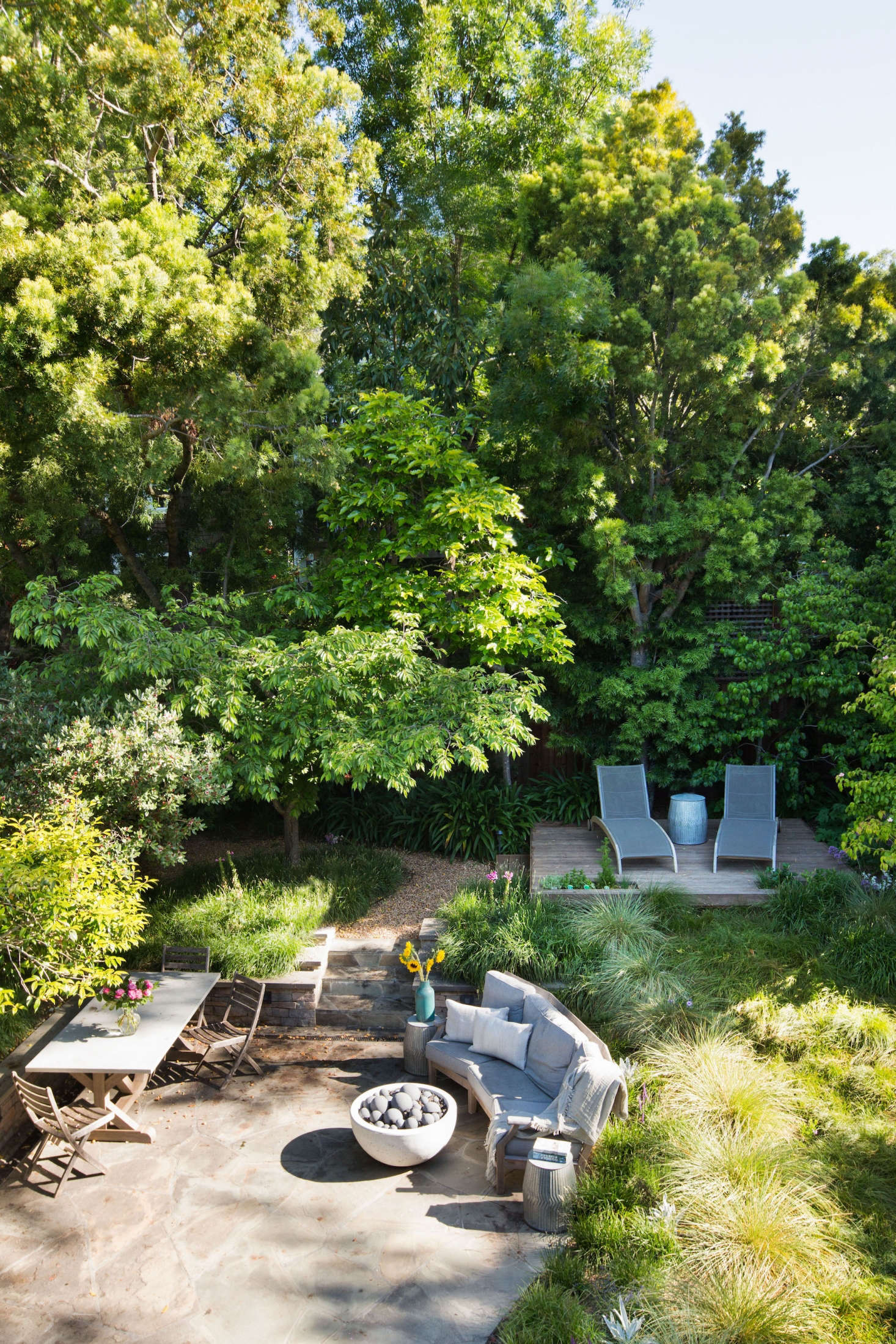 From a bedroom balcony, you look down into a backyard meadow full of flowing grasses. A raised wooden platform with lounge chairs is in the spot once occupied by a backyard trampoline.