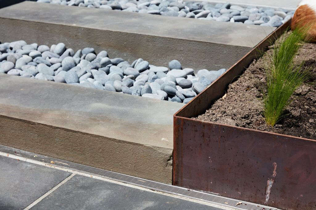 A set of bluestone and river rock steps connects the two levels of the patio. For continuity, Choe used the same bluestone from the upper patio; the rocks are La Paz beach pebbles. At right: the corner of the Cor-ten steel garden bed. (For more, see Landscaping Ideas: 8 Surprising Ways to Use Cor-ten Steel in a Garden.)