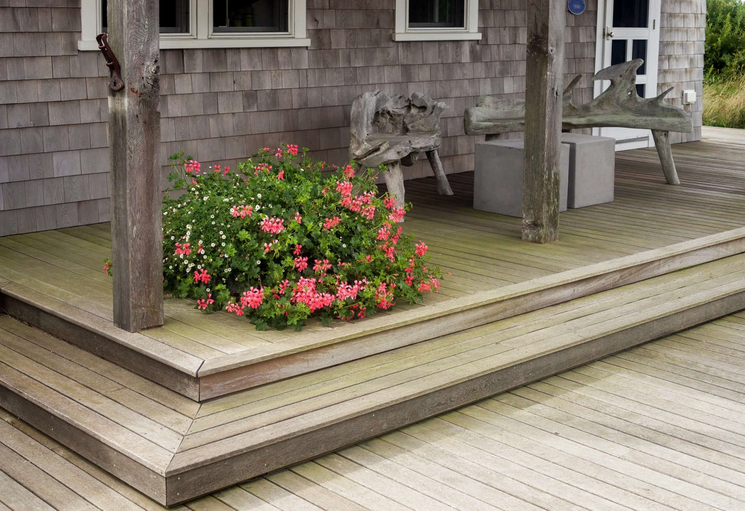 A colorful foil for the gray, weathered shingles on the porch of the original structure, Tim employed another signature element: generous and vibrant planters, this one planted with hot-pink Geranium 