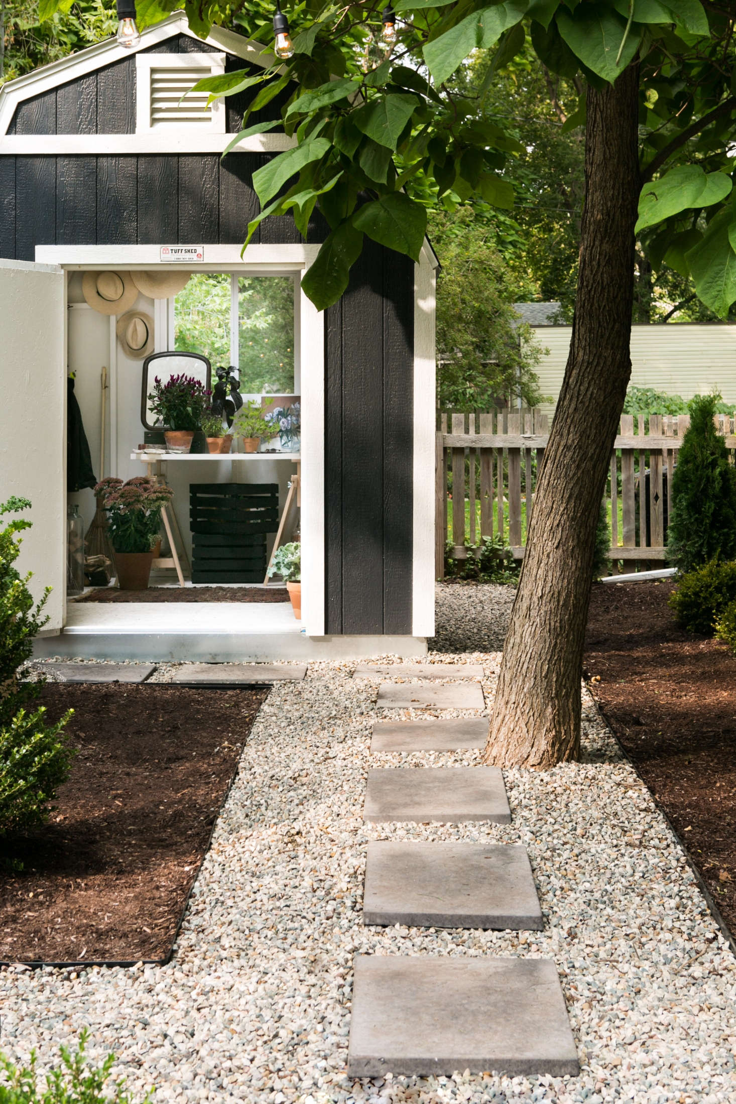A shed tucked into the back corner of the garden is linked visually with a path of pavers set in gravel. Adams installed a customized Tuff Shed from Home Depot, matching the facade color to the exterior paint on her house.