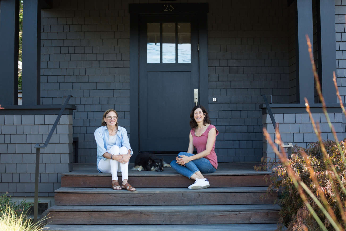 Haegglund (L) and Raleigh Zwerin sit on the front porch, where Arts and Crafts-inspired architectural accents include paired columns, a front door with window panes, and a waist-high railing.