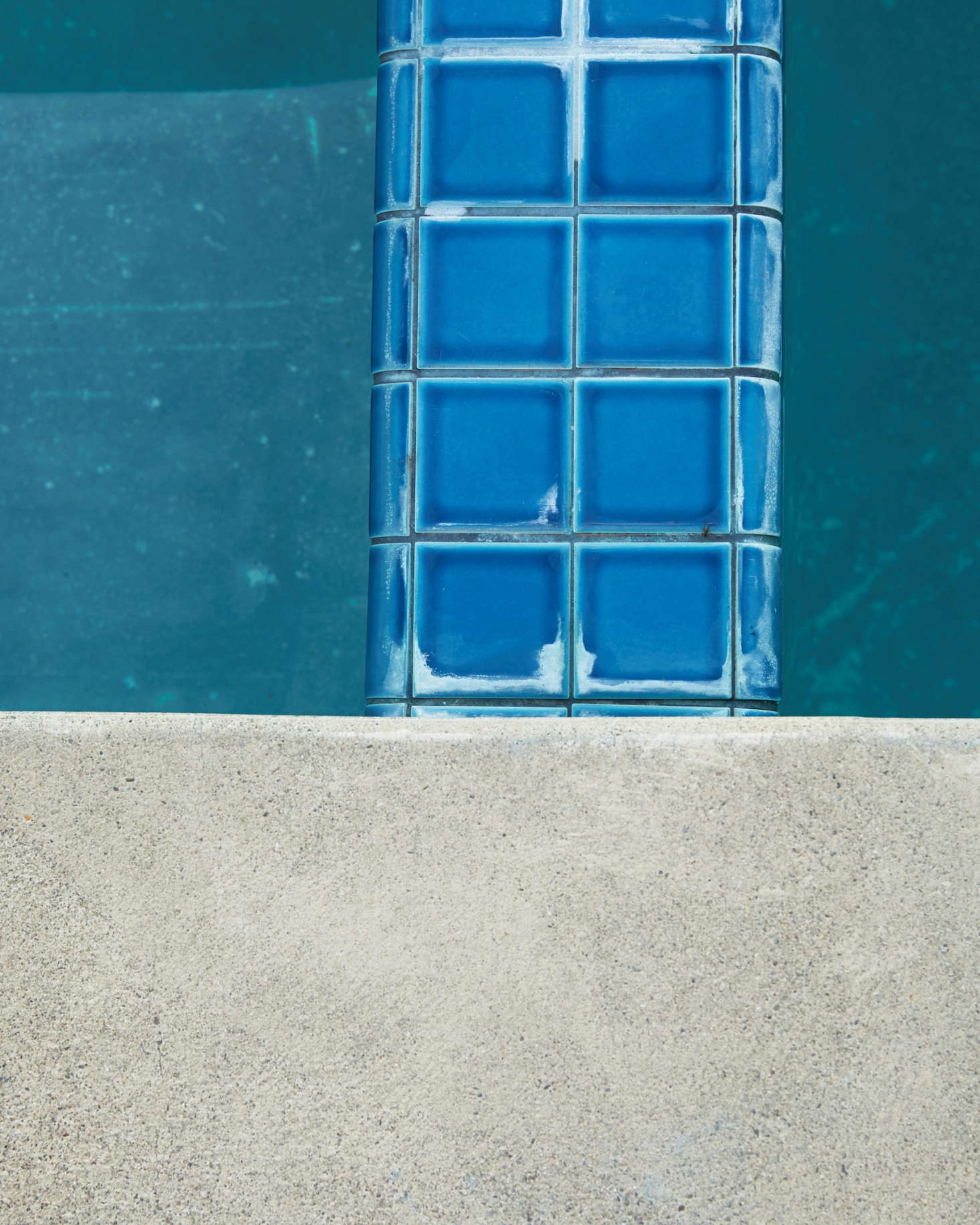 Bright turquoise tiles and a pale concrete deck define space in and around the dark teal pool.