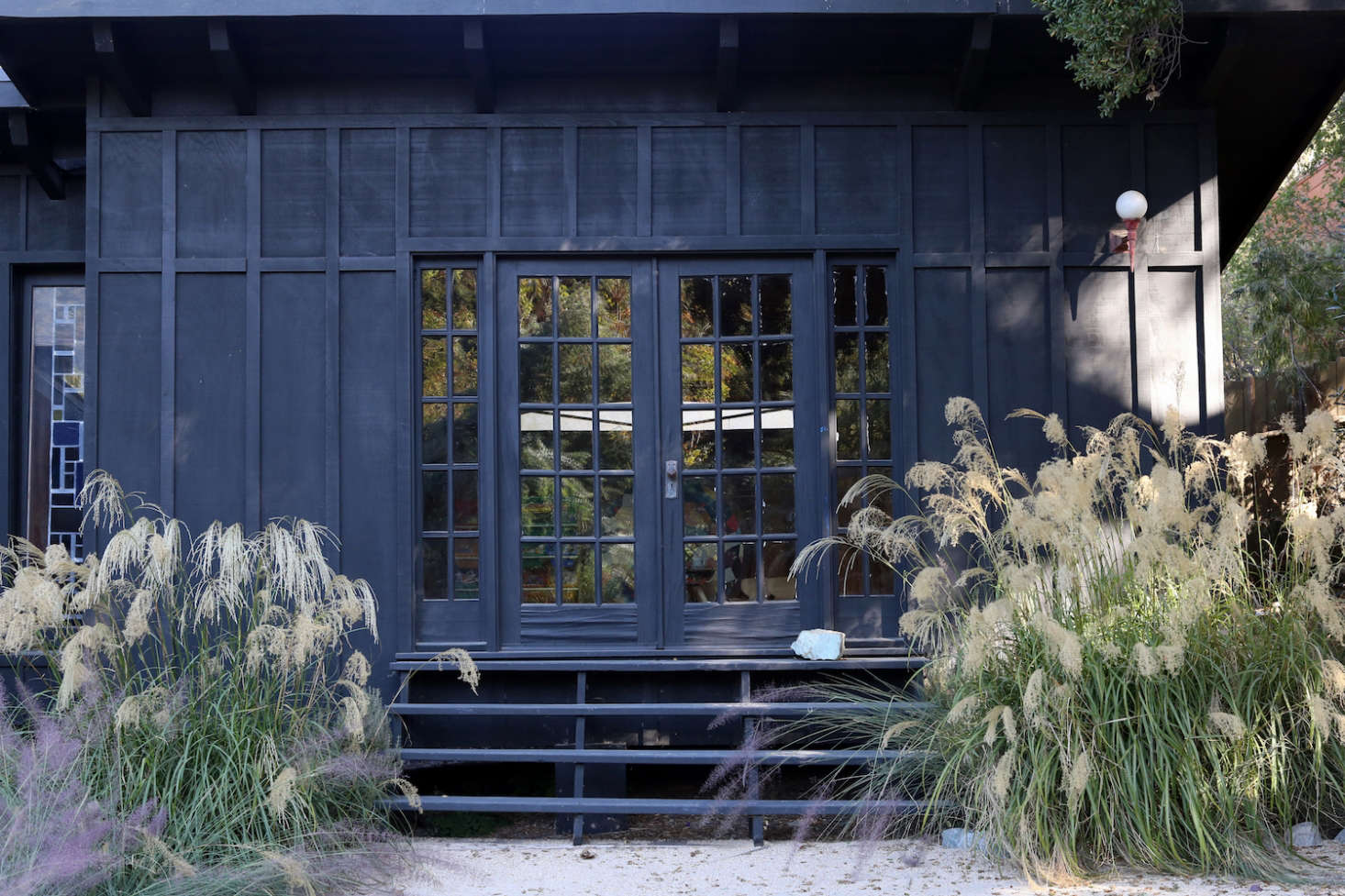 Two white grasses flank a short stairway and French doors on one end of the house.