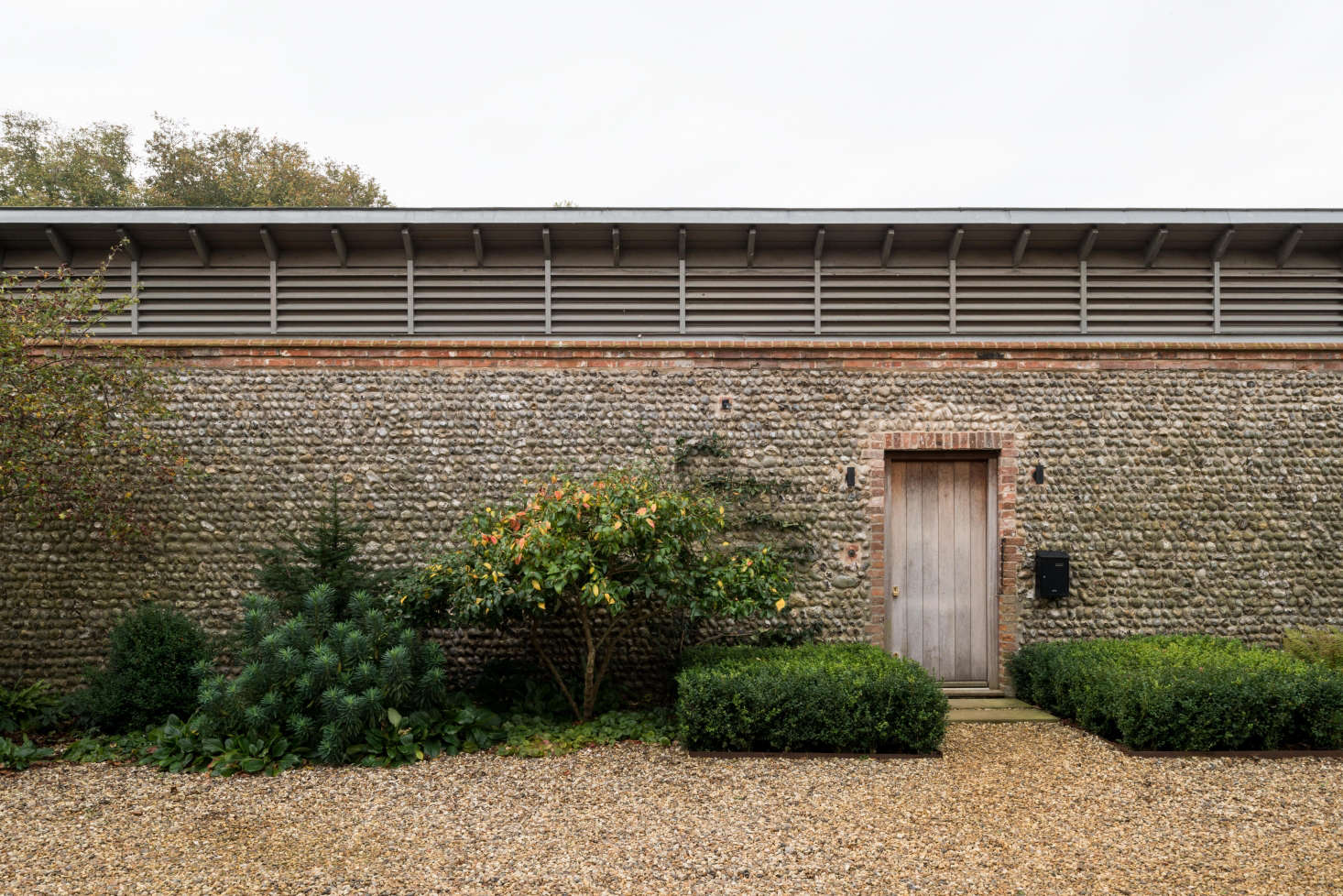 Against the flint facade of the piggery, Erlam planted a mix of shrubs and perennials such as euphorbia (at Left), edged by a gravel courtyard.