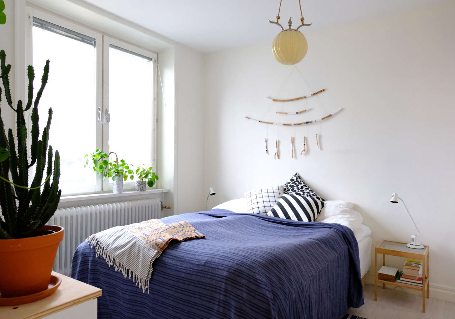 The bed faces the plant wall, which receives plenty of natural light. The interesting ceiling light came with the apartment. Maria made her branch wall hanging using paint and blue thread.