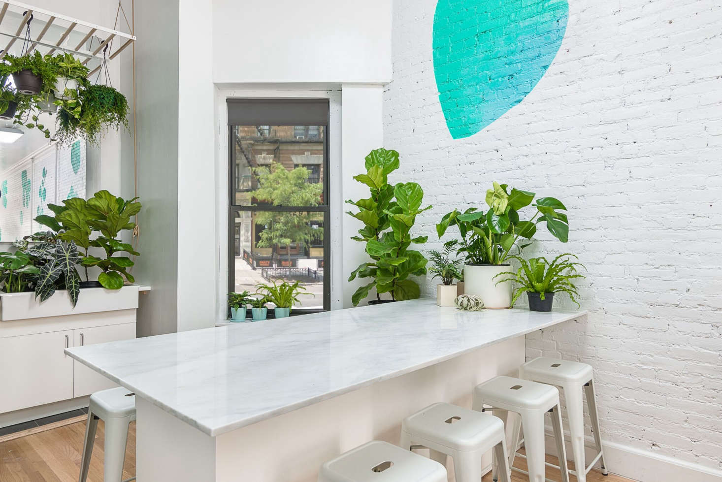 The shop has white brick walls that allow the greenery to stand out. A marble-topped bar/checkout area serves as a table for the shop