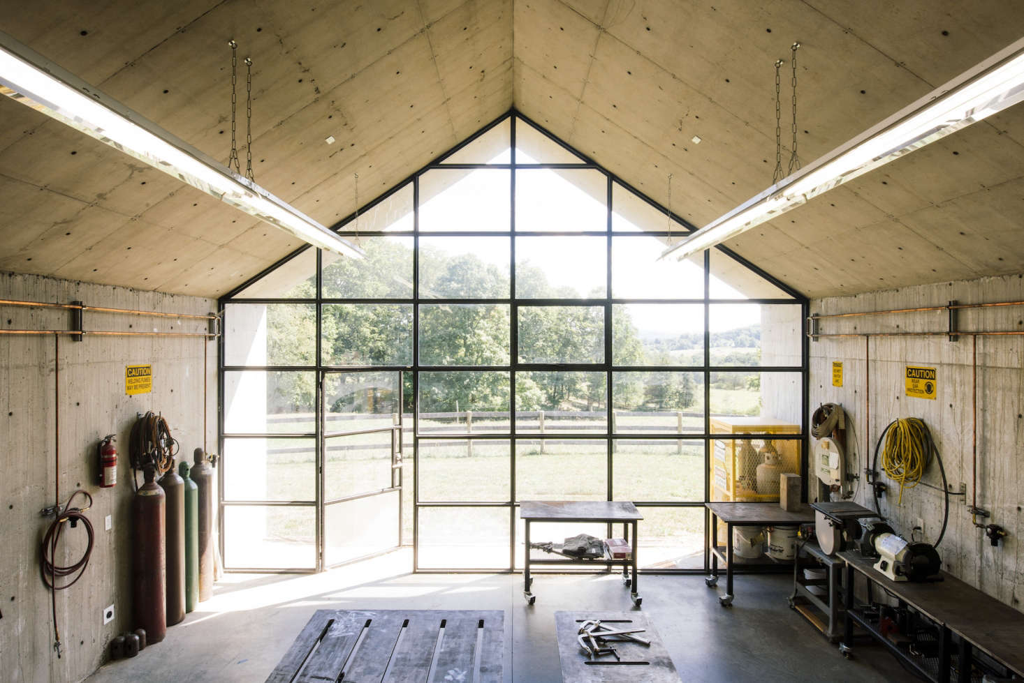 At one end of the studio is a gabled wall of gridded steel windows with embedded lights and an operable door. The studio is lighted by two long rows of off-the-shelf fluorescent hanging lights.