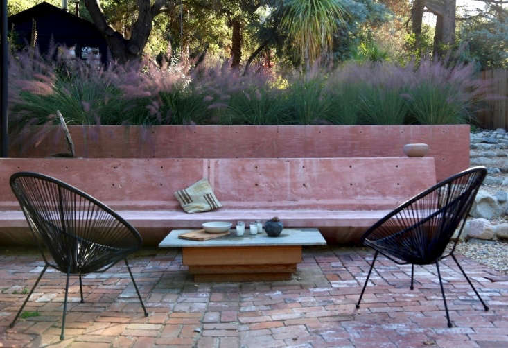 A long concrete bench juts out from the house, and defines the brick patio as an outdoor room. Matthew Morgan made the coffee table, which has a wood base with marble slab top. The black Acapulco chairs are from a garden store at the base of Topanga Canyon.