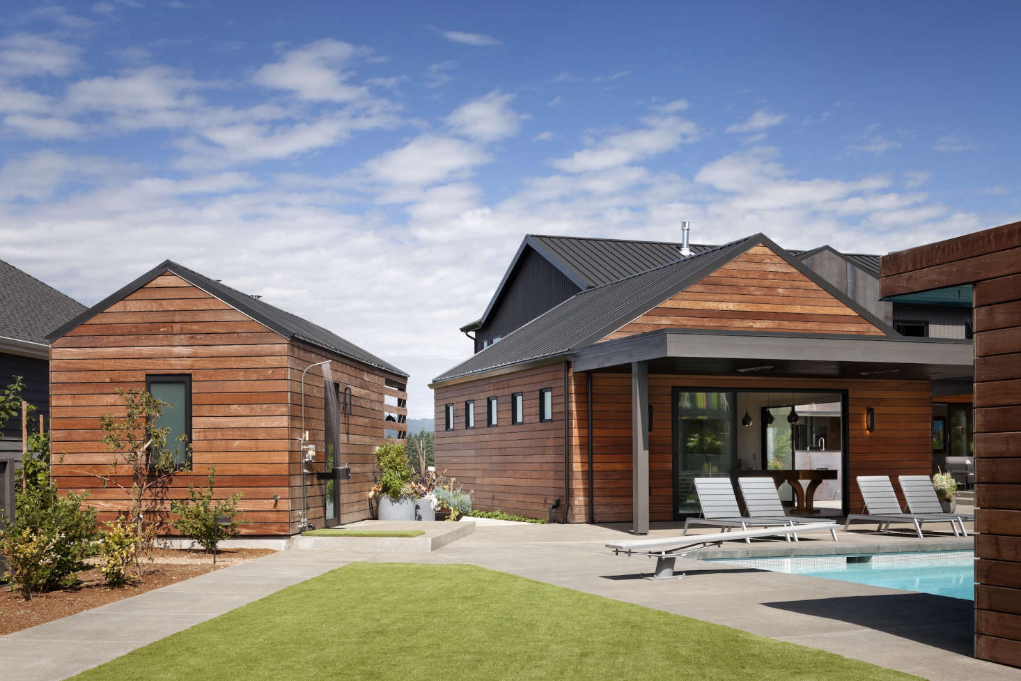 To the left of the media room is a detached pool house with a bathroom, storage space for pool equipment, an outdoor shower, and partially enclosed garden storage on the back side.