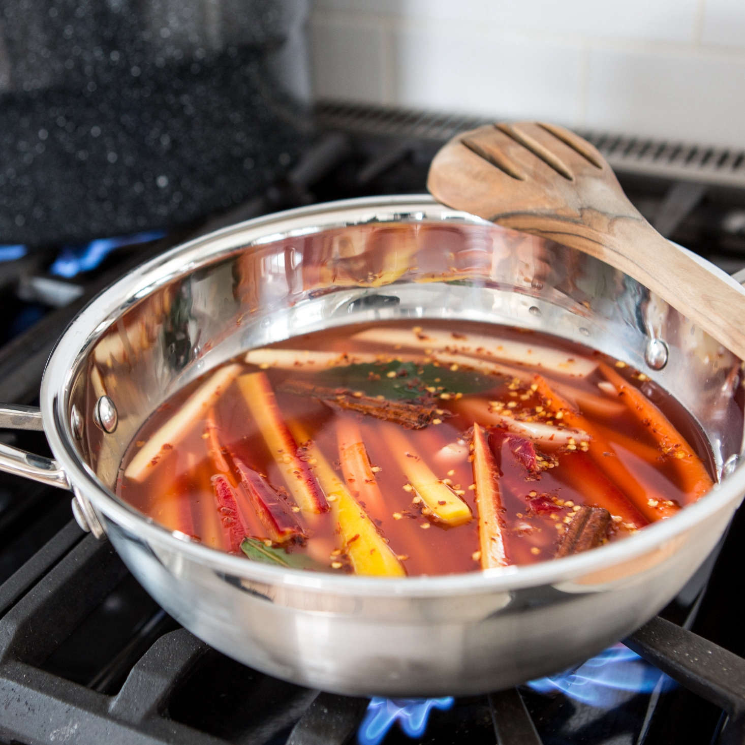 Vinegar, salt, maple syrup, spices, sliced garlic, and carrots simmer on the stovetop.