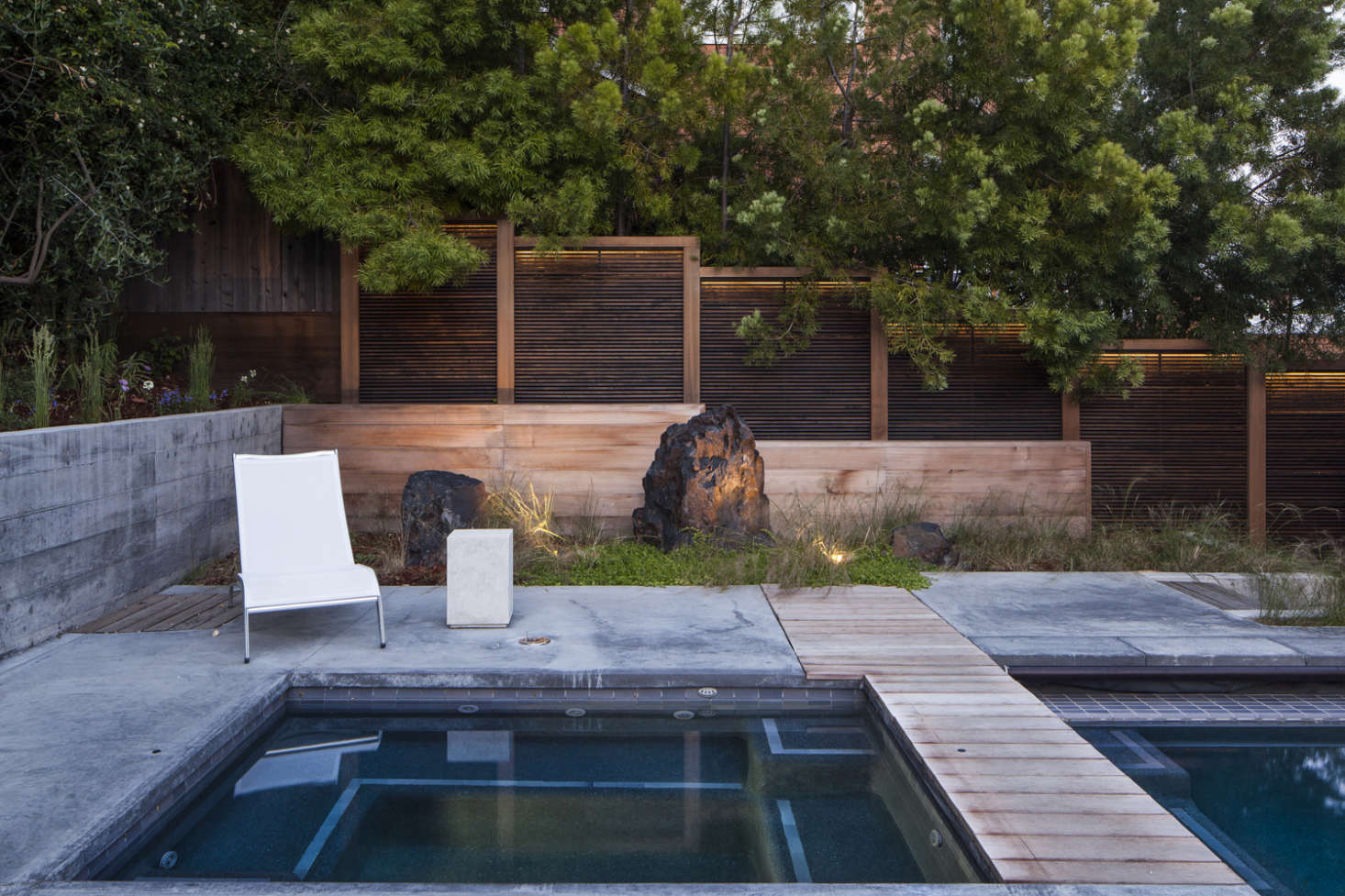 A stepped wood fence behind the pool is lit by warm-hued LED strips.