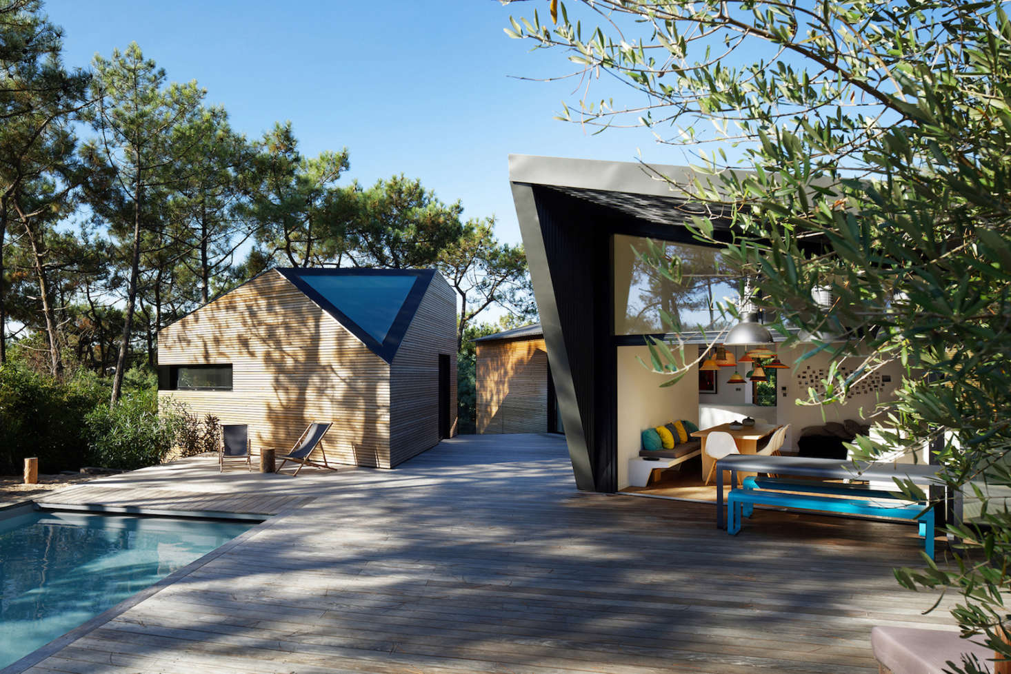 A shared living space in the building closest to the pool is sided in black lacquered, ribbed aluminum. It has full-height sliding doors that open onto the pool deck.