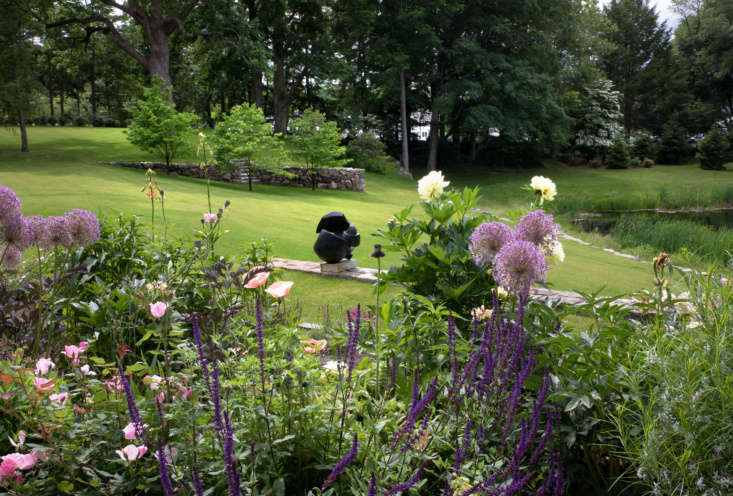 From the kitchen windows and adjacent pergola, the view encompasses both the cutting garden—with allium, geranium, heuchera, oriental poppy, delphinium, iris, rose, peony, and foxglove—as well as the pond and old stone wall beyond.