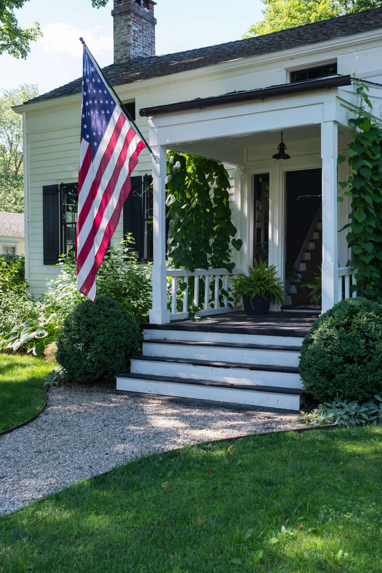 The front entrance, seldom used by the couple, with trailing potato vines casting shadows on the steps.