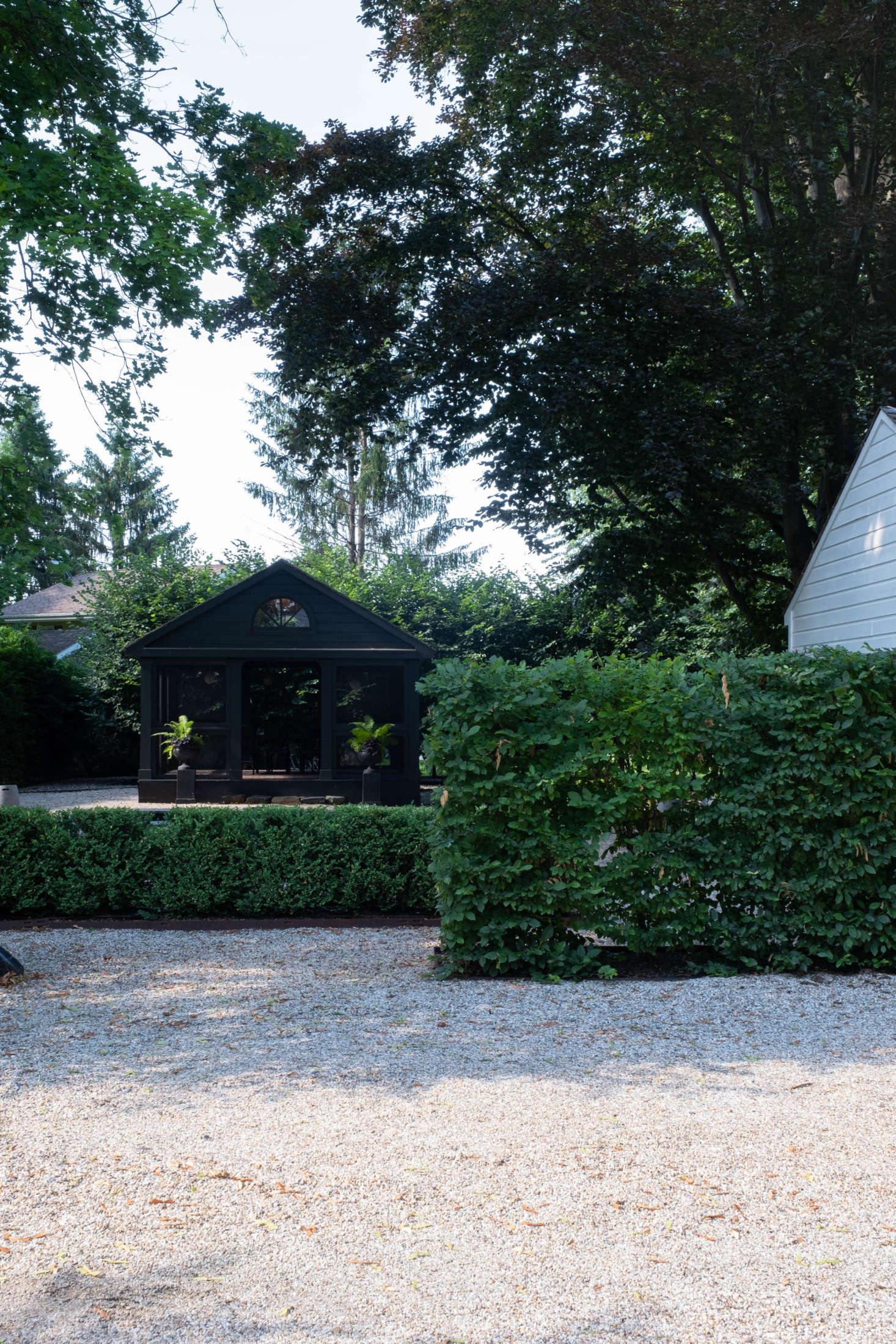 Adjacent to the patio, bordering the driveway, two rows of hornbeam hedges—one tall, one short—create a passage of sorts, leading into the expansive gravel garden.