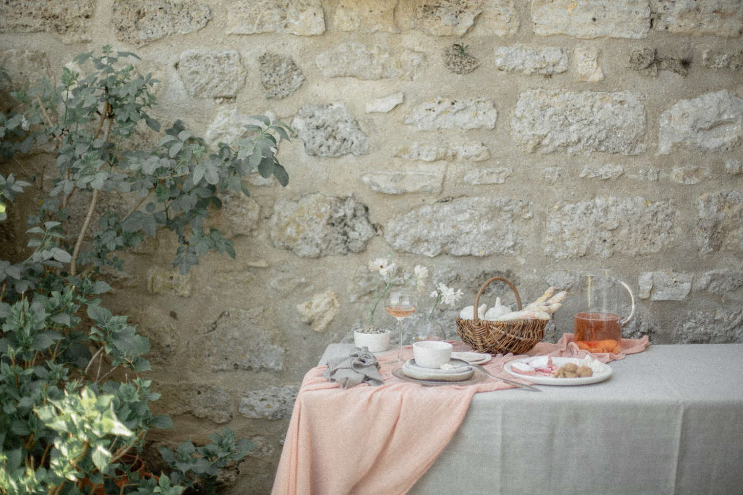 An undone-chic table at the French country house, set with summer drinks, freshly picked white asparagus, and a simple white floral arrangement.
