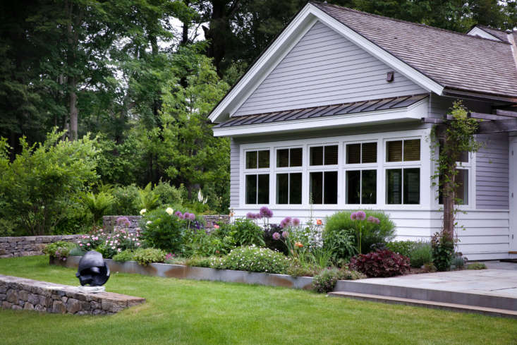 Fieldstone walls, inset in the gentle slope, provide a visual transition to other parts of the landscape. In the background, beyond the wall, native plants such as ostrich fern (Matteuccia struthiopteris) dominate and provide a transition to the wooded area.