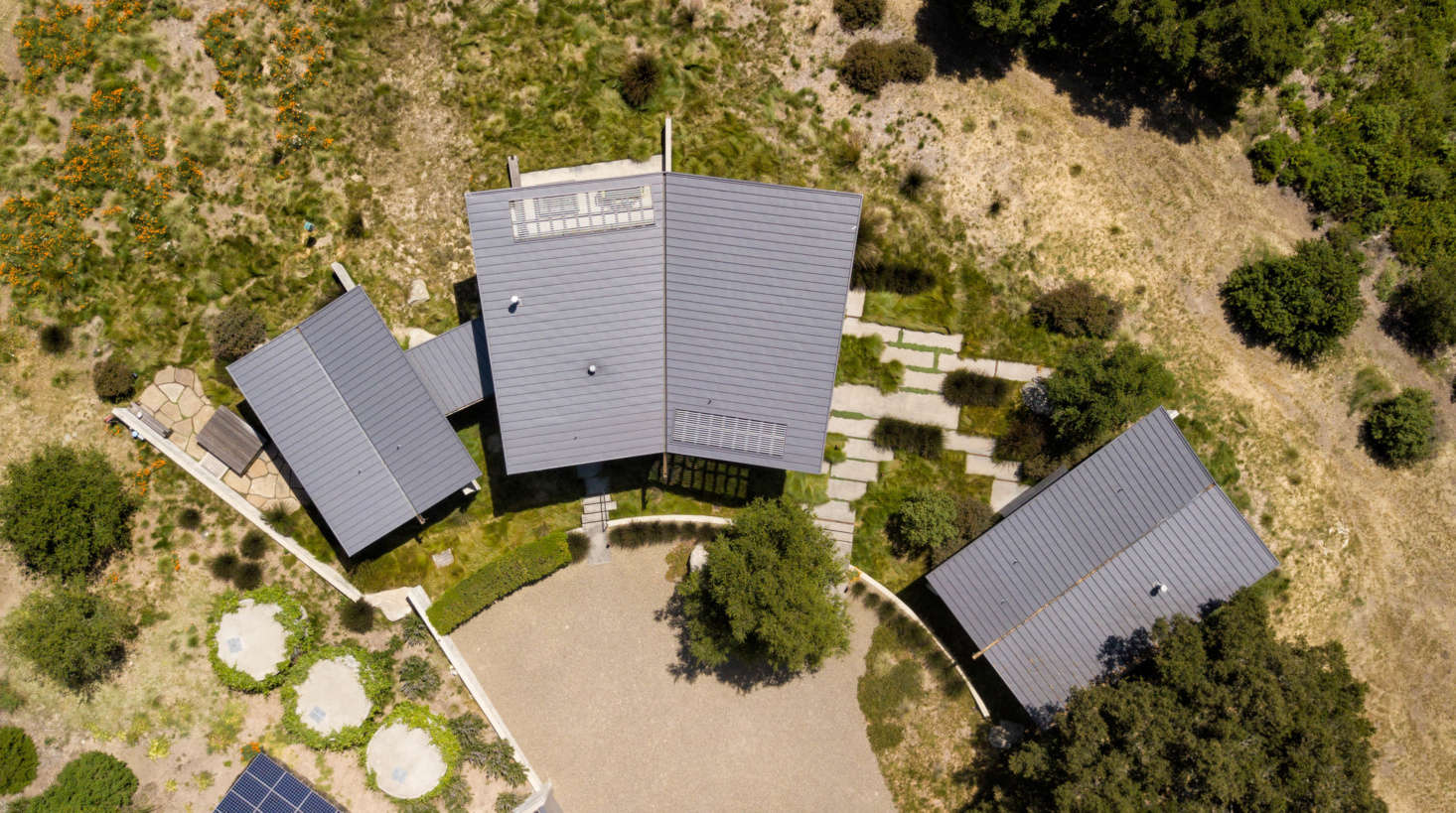 Armed with an engineering report from Sheerline Structural Engineering, the team designed a gravel autocourt to prevent rainwater runoff and board-formed concrete walls (at Left) to create a visual buffer between the house and a trio of concrete rainwater harvesting tanks.