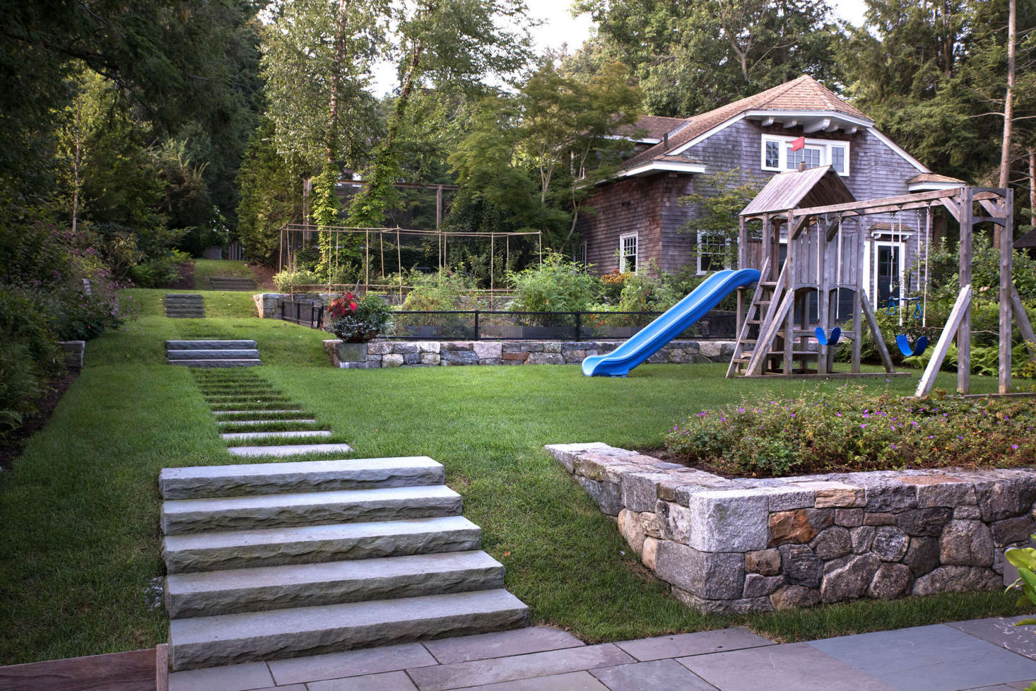 Though it it looks like a single, cohesive space, the backyard actually has a series of five gently graded terraces. At various elevations are a tennis court (behind the garage); an upper garden with a fountain and berry patch; a lower kitchen garden; a play lawn, and (shown in the foreground) a patio next to the house. Newly constructed hardscaping, including low stone walls and bluestone pathways, defines each distinct space and creates visual unity.