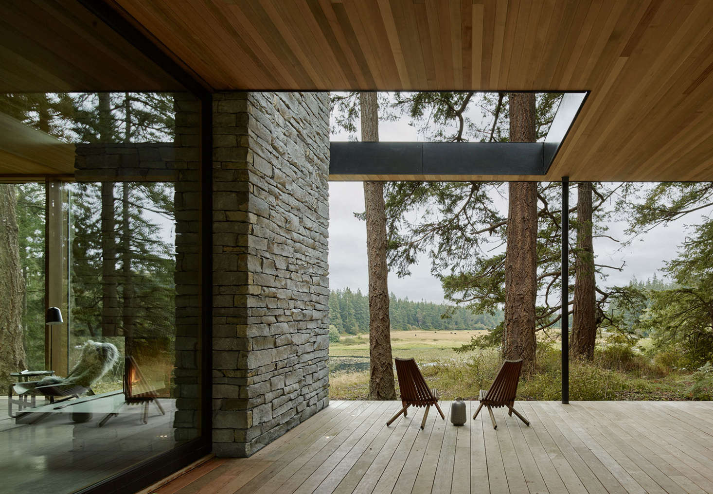 An indoor fireplace transitions into the exterior stone wall of a picturesque deck by mwworks. Photograph by Kevin Scott, courtesy of mwworks, from Outside In: A Multi-Generational Retreat on Whidbey Island Welcomes Nature Inside.