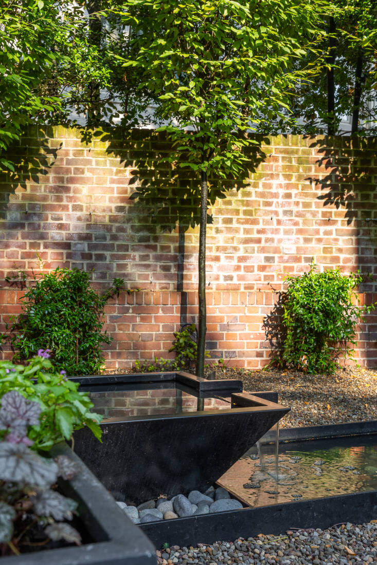 A Bobé water bowl with a bubbler feeds into the custom powder-coated steel basin. The water bowl matches the fire table (also by Bobé in the nearby seating area). Jasmine will eventually climb the brick wall.