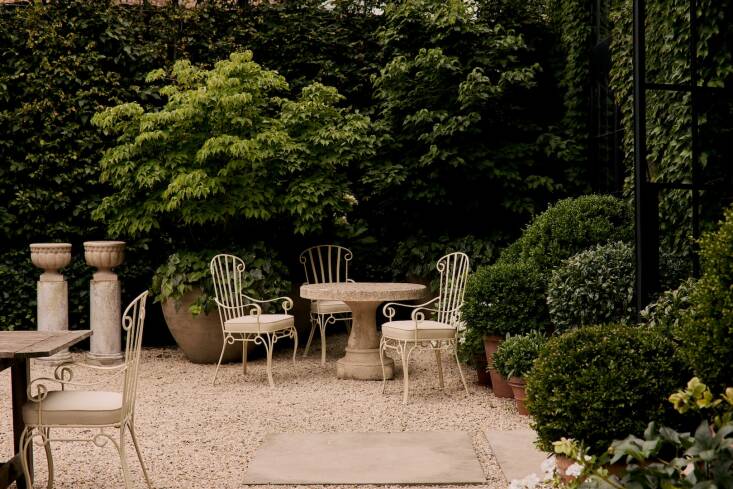 A set of four \1950s Sculptural Wrought Iron Armchairs of refinished metal with new outdoor-safe seat cushions. The circular French Modernist Cast Stone Table dates from the \1960s. The round planters on plinths are midcentury French Cast Stone Garden Urns.