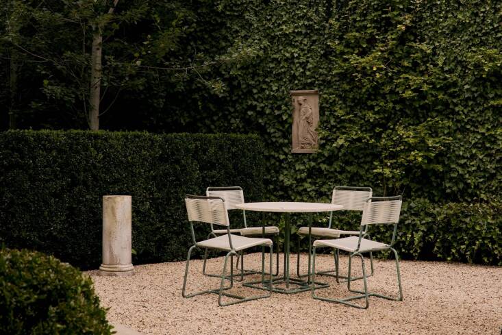 A \1950s Brown Jordan Walter Lamb Bronze Patio Set: the four chairs have been restrung and the café table is newly topped with a weathered travertine slab. The goddess relief in the background is a Concrete Depiction of Gradiva Plaque.